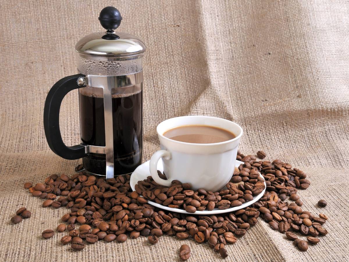 French press. Przeczytaj o tym prostym urządzeniu do zaparzania kawy 1 Kawa z french press, filiżanka i ziarna rozsypane. Obrazek w artykule French press - przeczytaj o tym prostym urządzeniu do zaparzania kawy